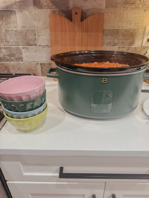 green crock pot and multicolor bowls are sitting on kitchen counter.