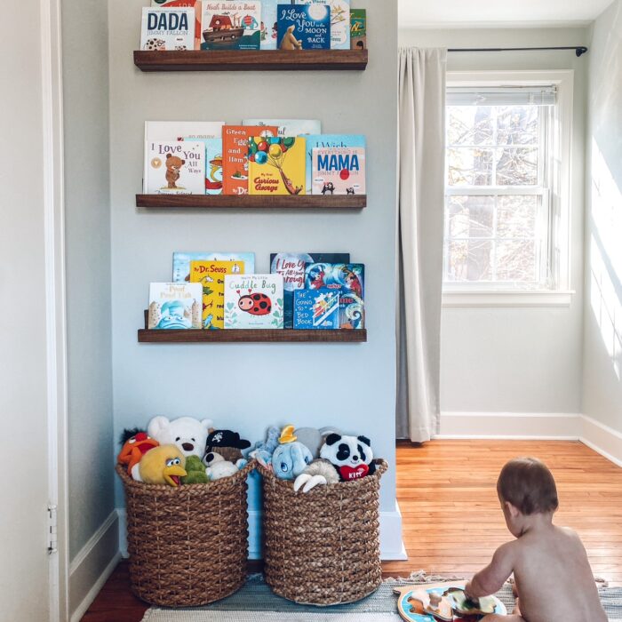 Baby boy nursery, seagrass baskets with stuffed animals, walnut stained wood floating bookshelves, children's books, striped rug