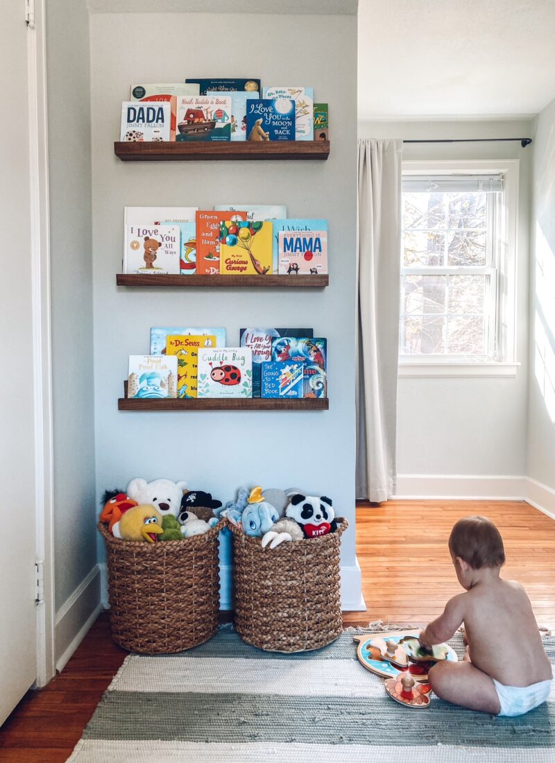Baby boy nursery, seagrass baskets with stuffed animals, walnut stained wood floating bookshelves, children's books, striped rug