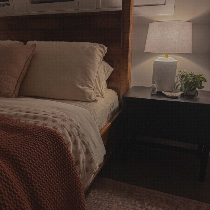 cozy bedroom with white table lamp, house plant, and linen spray on the black nightstand.